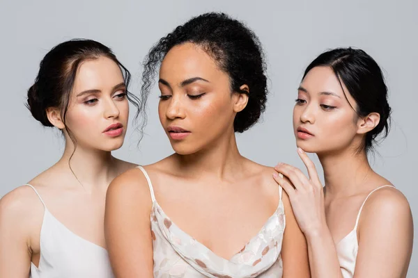 Pretty multiethnic friends in satin dresses standing isolated on grey — Stock Photo