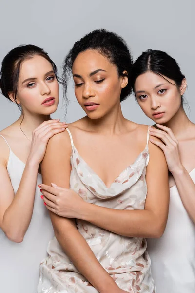 Pretty brunette interracial women touching african american friend isolated on grey — Stock Photo