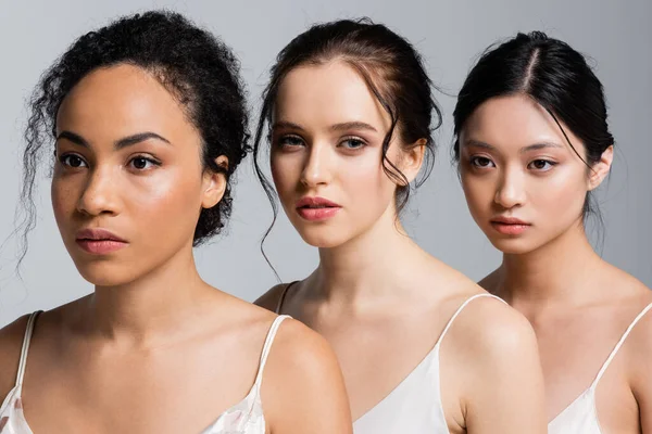 Young woman in satin dress looking at camera near multiethnic friends isolated on grey — Stock Photo