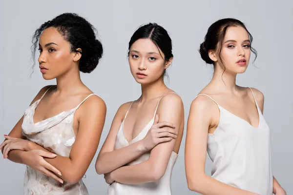 Hübsche Asiatin im Satinkleid steht neben multiethnischen Frauen isoliert auf grau — Stockfoto