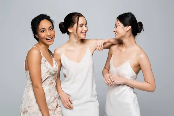 Positive multiethnic women in satin dresses standing isolated on grey — Stock Photo