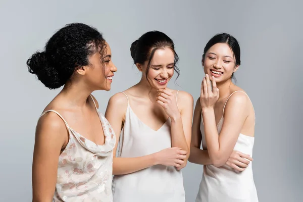 Cheerful multicultural women with perfect skin closing eyes isolated on grey — Stock Photo