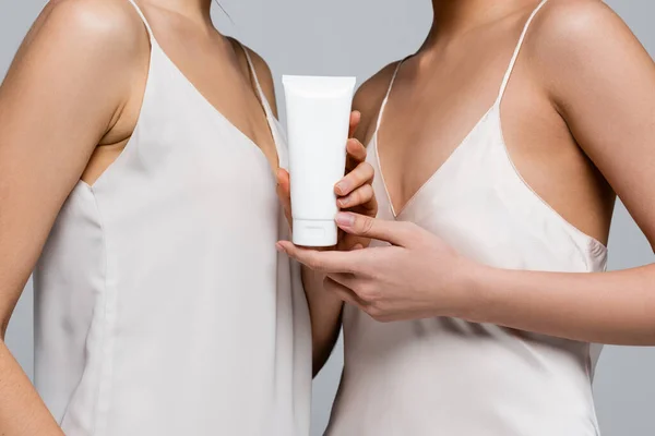 Cropped view of women in satin dresses holding cream in tube isolated on grey — Stock Photo