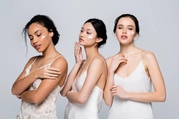 Jolies femmes interracial avec de la crème sur les visages isolés sur le gris — Photo de stock