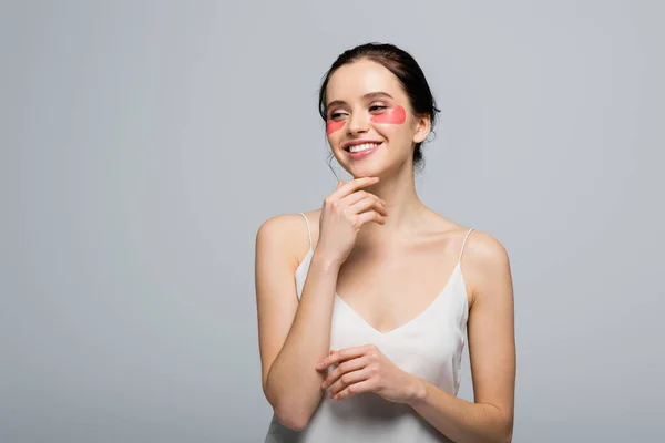 Mujer joven y bonita con parches en los ojos mirando hacia otro lado aislado en gris - foto de stock