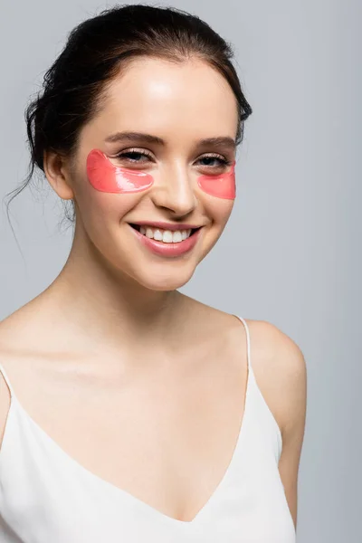 Portrait of smiling woman with eye patches looking at camera isolated on grey — Stock Photo