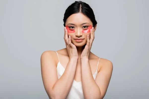 Jolie jeune femme asiatique avec des patchs pour les yeux regardant la caméra isolée sur gris — Photo de stock