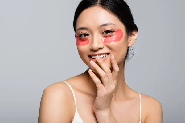 Hübsche asiatische Frau mit Augenklappen lächelt in die Kamera isoliert auf grau — Stockfoto