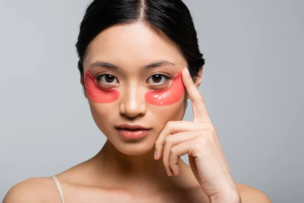 Pretty asian woman in eye patches looking at camera isolated on grey — Stock Photo