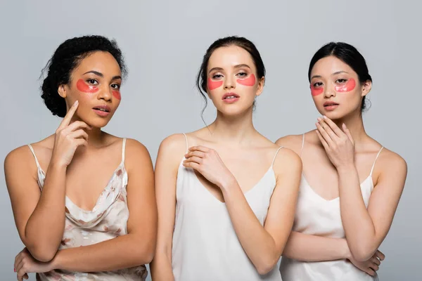 Mujeres interraciales con parches en los ojos mirando a la cámara aislada en gris - foto de stock