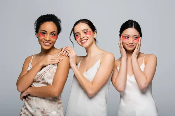 Lächelnde multiethnische Frauen mit Augenklappen, die isoliert auf grau in die Kamera schauen — Stockfoto