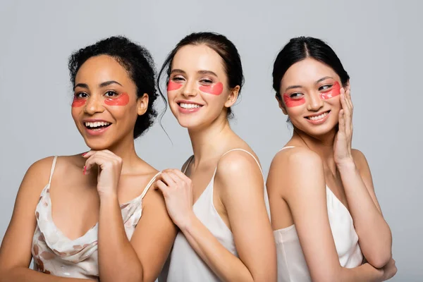 Mujeres multiculturales felices con parches oculares de pie aislados en gris - foto de stock