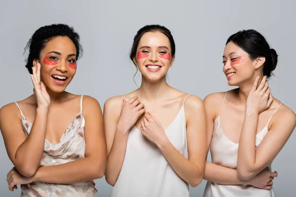 Happy interracial women with eye patches standing isolated on grey — Stock Photo