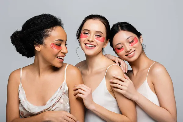 Glückliche multiethnische Frauen mit Augenklappen, die sich vereinzelt auf grau umarmen — Stockfoto