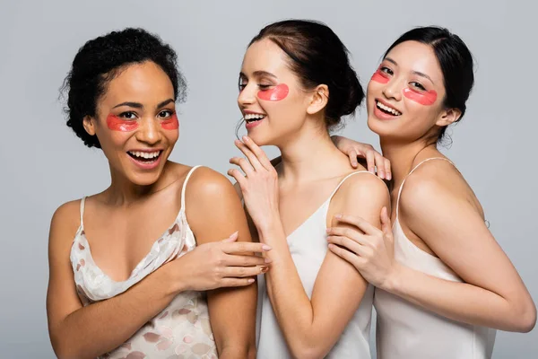 Mujer afroamericana sonriente con parches en los ojos cerca de amigos multiétnicos aislados en gris - foto de stock