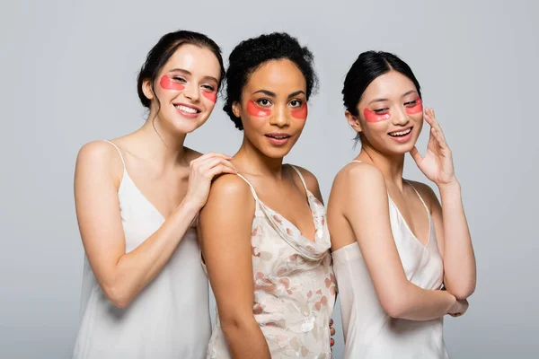 Junge und hübsche interrassische Frauen in Augenklappen stehen isoliert auf grau — Stockfoto