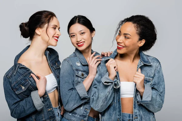 Pretty multicultural women with red lips looking at each other isolated on grey — Stock Photo