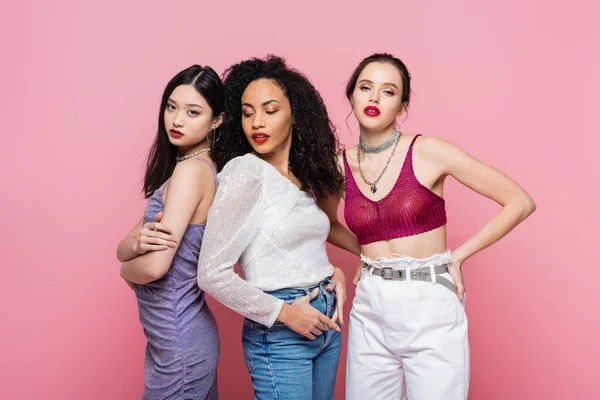 Jóvenes mujeres multiétnicas posando durante el partido aisladas en rosa - foto de stock