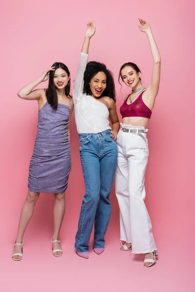 Volle Länge fröhlicher multikultureller Frauen, die auf rosa Hintergrund in die Kamera schauen — Stockfoto