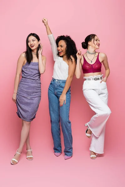 Повна довжина щасливих мультикультурних жінок, які позують під час вечірки на рожевому фоні — стокове фото