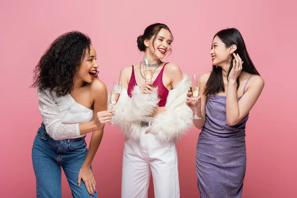 Mulheres multiétnicas sorridentes segurando copos de champanhe isolados em rosa — Fotografia de Stock