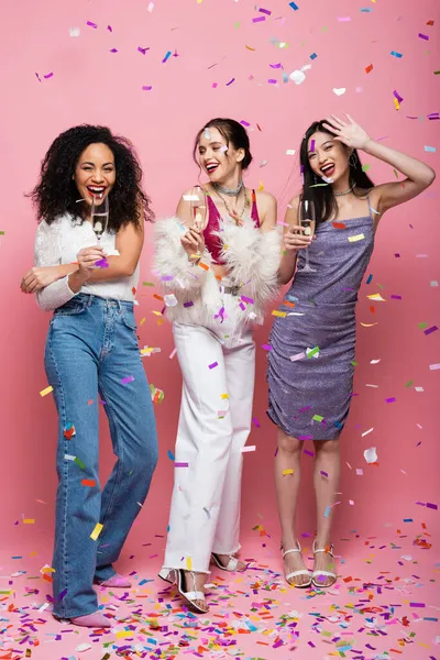 Asian woman waving hand near interracial friends with champagne on pink background — Stock Photo