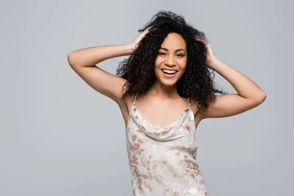 Positive african american woman touching hair isolated on grey — Stock Photo