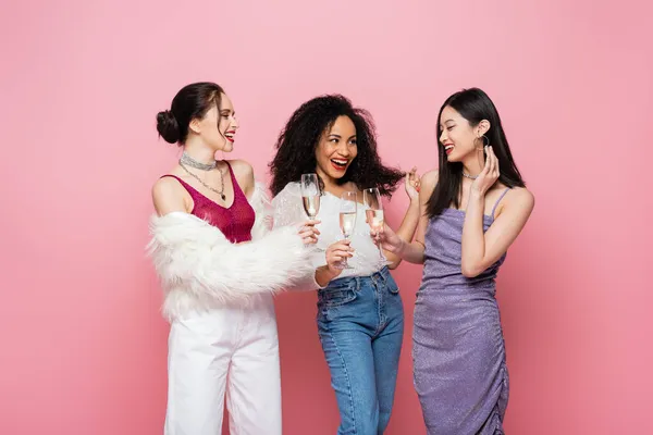 Sonrientes amigos multiculturales brindando con champán aislado en rosa - foto de stock