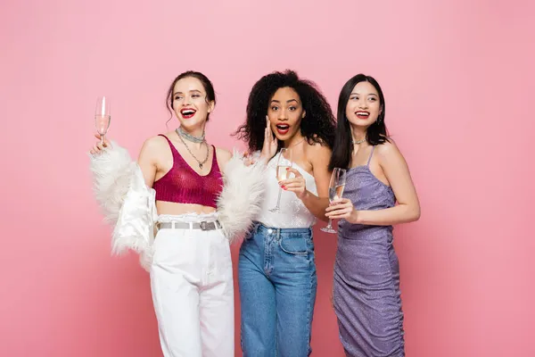 Excited african american woman holding champagne near cheerful interracial friends isolated on pink — Stock Photo