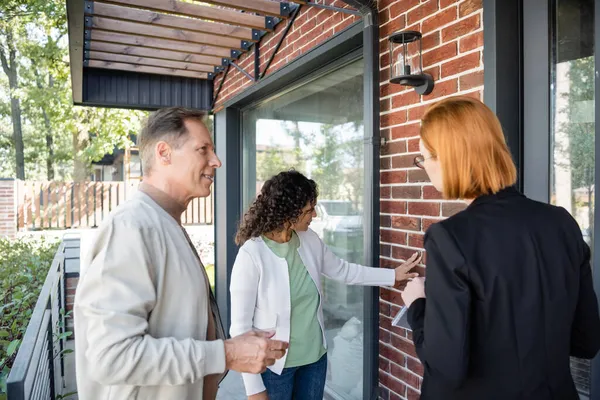 Redhead realtor showing modern house to happy multiethnic couple — Stock Photo
