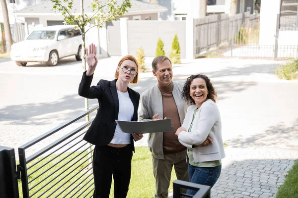 Realtor with folder pointing away near happy husband and african american wife — Stock Photo