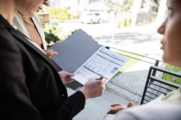 Borrosa inmobiliaria celebración de pluma y carpeta con solicitud de préstamo cerca de la mujer y el hombre - foto de stock