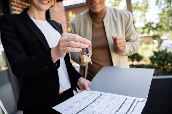 Partial view of cheerful realtor holding key near blurred and happy man — Stock Photo