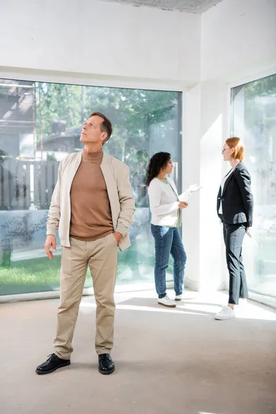 Man standing with hand in pocket near african american woman talking with redhead realtor — Stock Photo