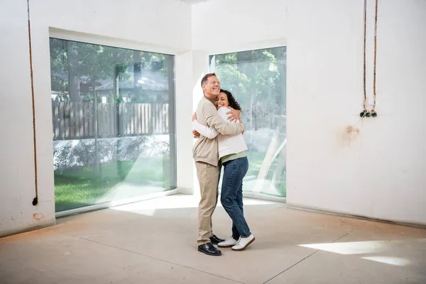 Felice uomo abbracciare compiaciuto afro americano moglie in nuova casa — Foto stock