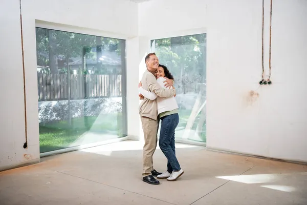 Happy man hugging pleased african american wife in new house — Stock Photo