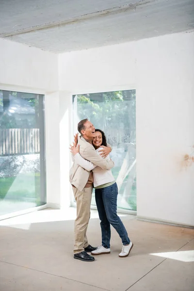 Веселий чоловік обіймає задоволену афроамериканську дружину в новому будинку — стокове фото
