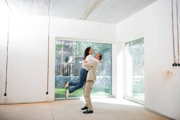 Homem alegre levantando mulher afro-americana satisfeito na nova casa — Fotografia de Stock