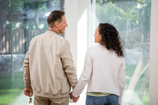 Веселий чоловік тримає ключ і дивиться на афроамериканську дружину в новому будинку — стокове фото