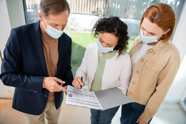 Donna afroamericana in maschera medica firma contratto vicino agente immobiliare e rossa fidanzata — Stock Photo