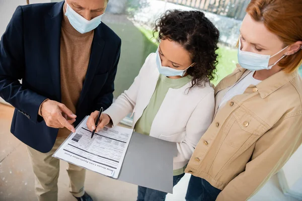 Donna afro-americana in maschera medica firma contratto vicino agente immobiliare e fidanzata — Foto stock