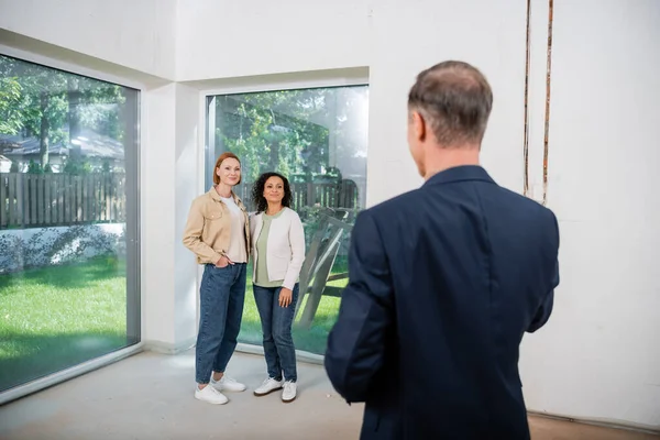 Interracial lesbian couple looking at blurred realtor in modern house — Stock Photo