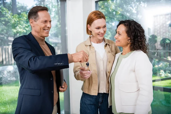 Positive realtor giving key to interracial lesbian couple inside of new house — Stock Photo
