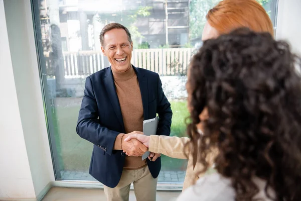 Happy realtor shaking hands with blurred redhead woman near african american girlfriend — Stock Photo