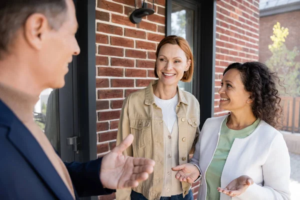 Blurred realtor gesturing near interracial lesbian couple — Stock Photo