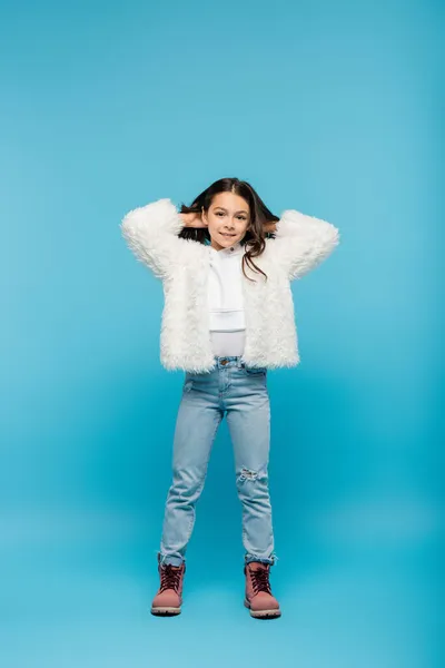 Longitud completa de la niña preadolescente feliz en chaqueta de piel sintética posando en azul - foto de stock