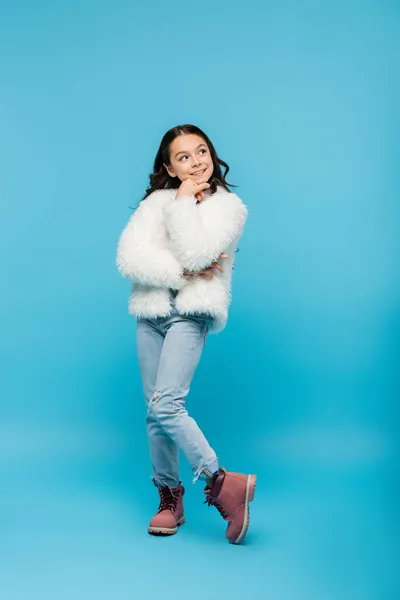 Full length of cheerful preteen girl in faux fur jacket posing on blue — Stock Photo