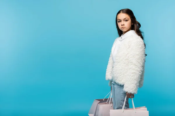 Preteen girl in white faux fur jacket holding shopping bags on blue — Stock Photo