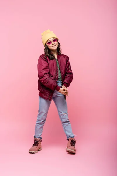 Full length of happy preteen girl in trendy outfit and sunglasses on pink — Stock Photo