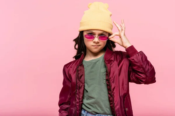 Preteen girl in trendy outfit adjusting sunglasses isolated on pink — Stock Photo